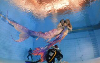 Zwei Mermaids schwimmen über Tauchern im Becken